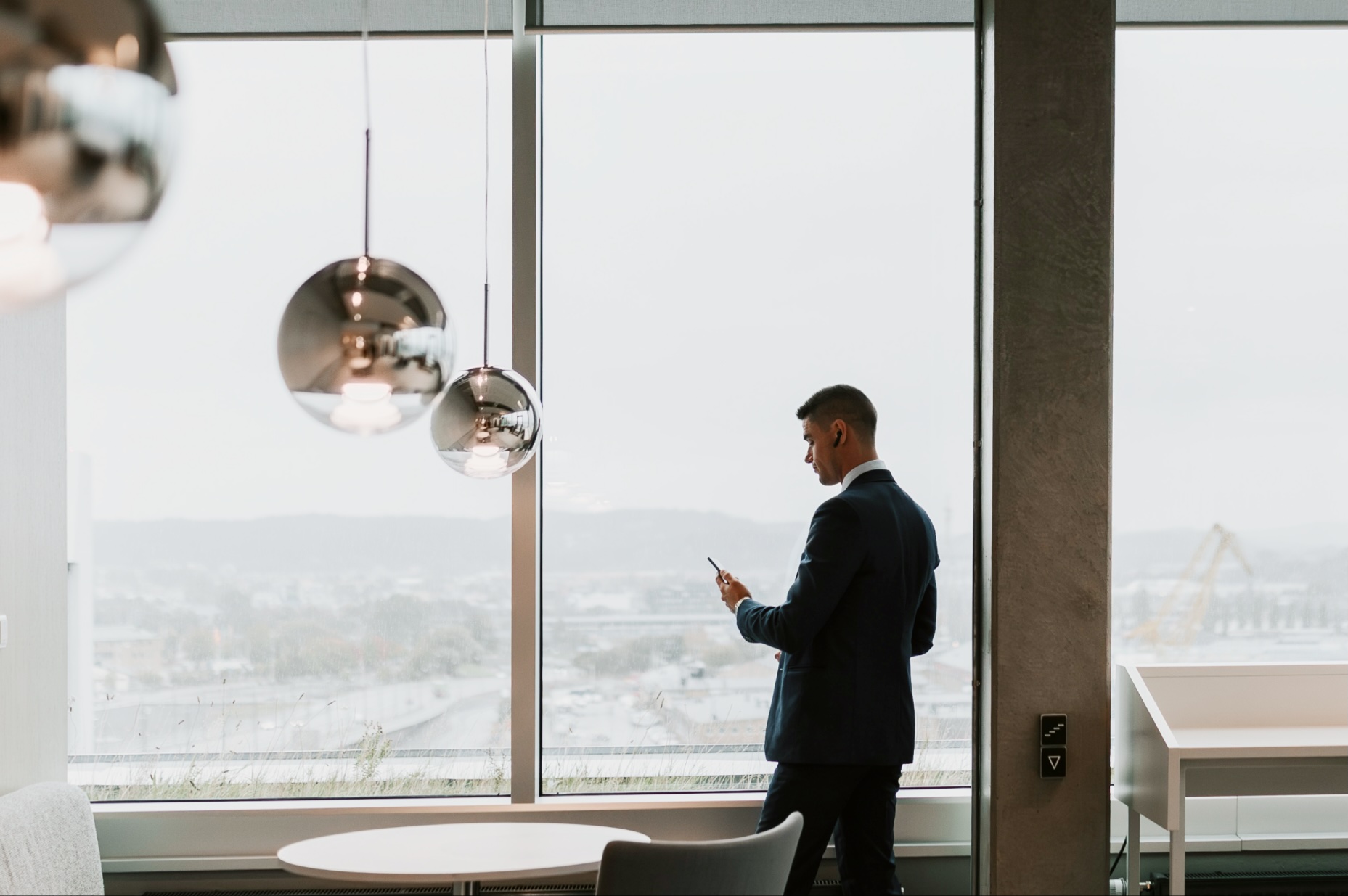 Man in a suit using his phone by the windows of a modern office.